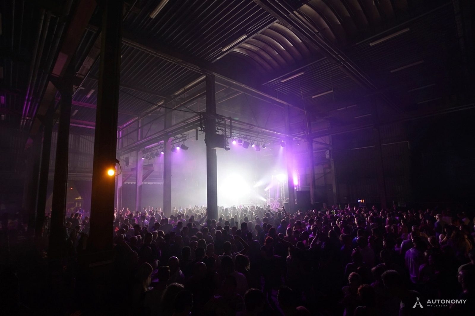Crowd facing a concert stage lit with purple and white lights