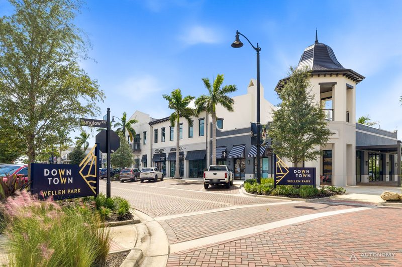 Downtown Wellen entrance sign on a brick-paved Main Street with palms and shopfronts