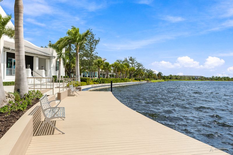 Wide lakeside promenade with a bench and palms along the Grand Lake in Wellen Park