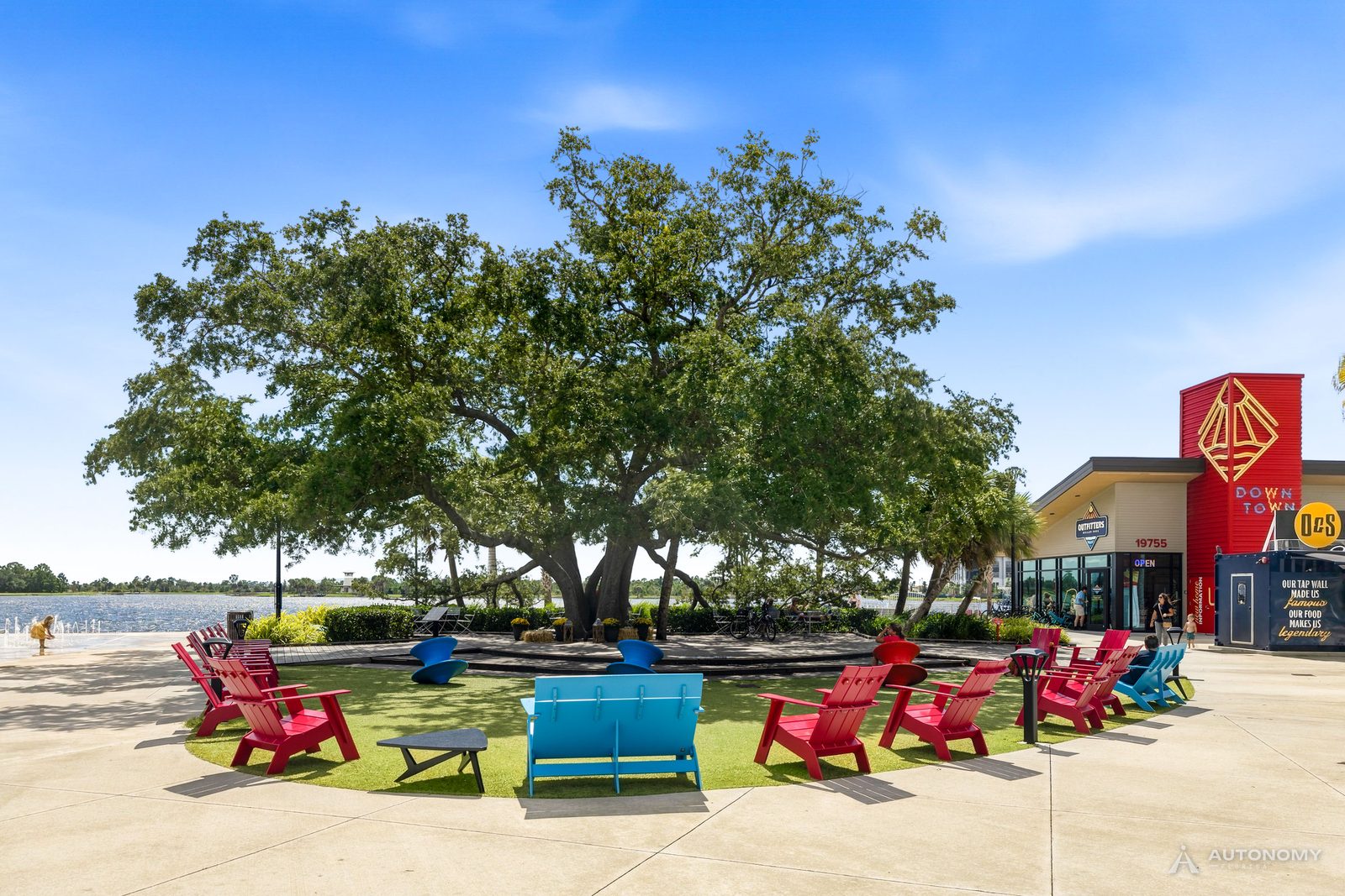 Heritage Tree oak with red Adirondack chairs beside the Grand Lake in Wellen Park