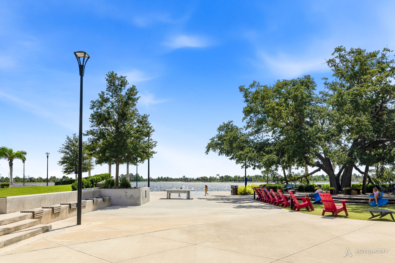 Red Adirondack chairs under oak trees on the Downtown Wellen lakefront plaza by the Grand Lake